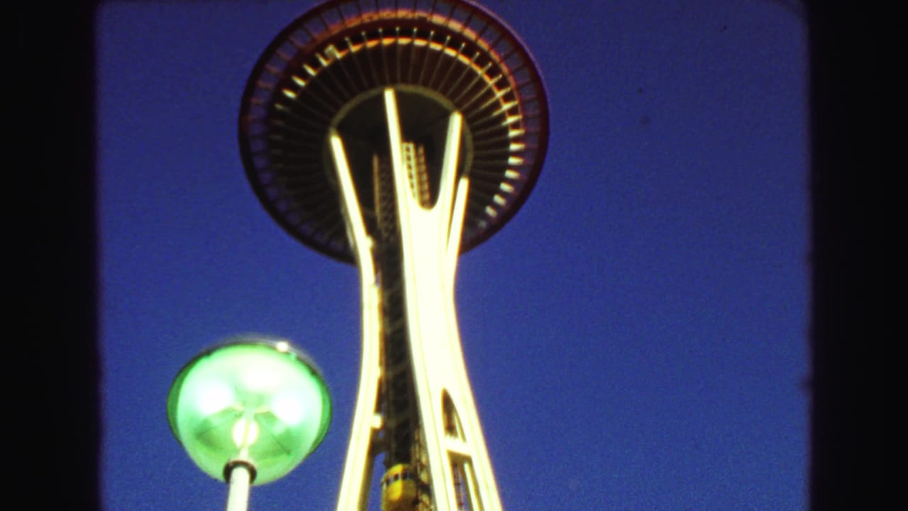 Low-angle view of a saucer-topped tower with a glowing green streetlamp against blue sky.