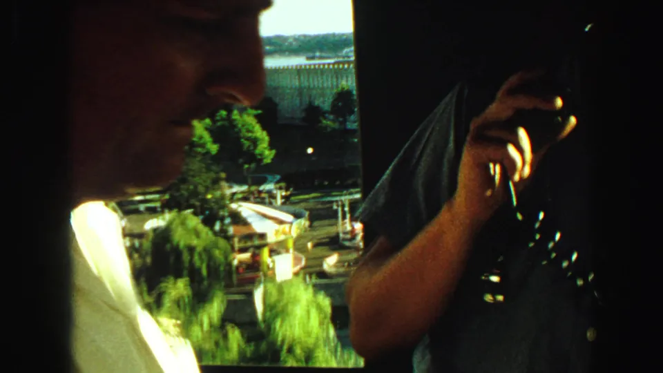 Inside the observation deck, one adult man holds a camera while another is seen in profile against a bright outdoor city view.