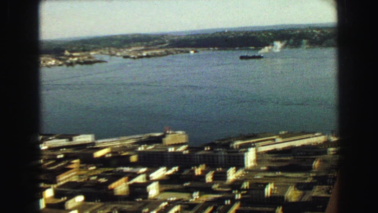 1968 8mm view over Vancouver waterfront with bay water, industrial docks, city buildings, and a ship on the horizon.