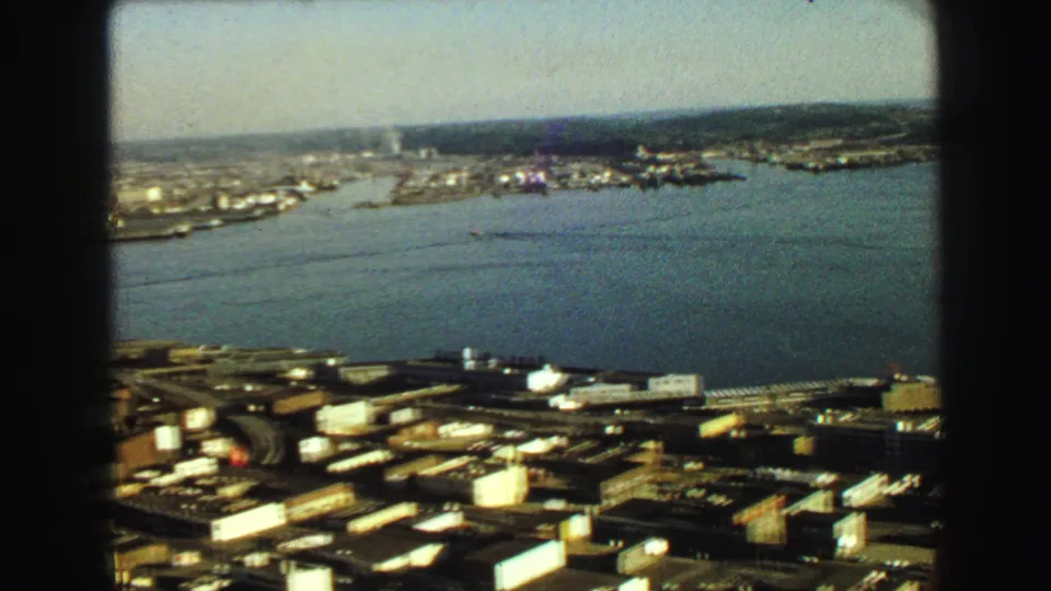 1968 8mm elevated view of Vancouver waterfront, with roads and buildings in the foreground and harbor water beyond.