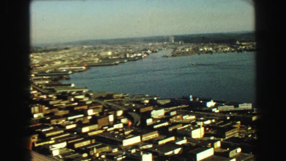 1968 Vancouver waterfront panorama showing urban blocks, dock areas, open harbor water, and distant industrial shoreline.