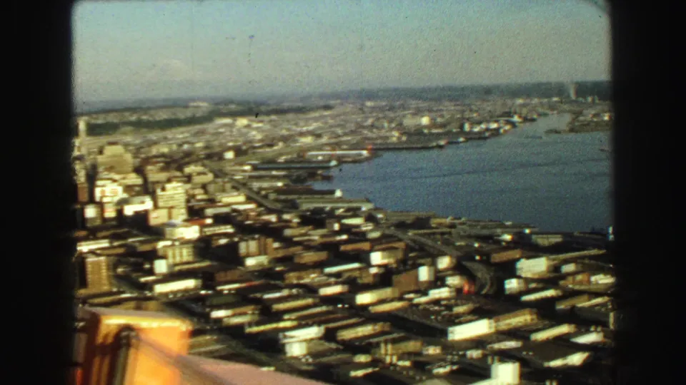 1968 8mm aerial view of Vancouver's waterfront, city blocks, transport corridors, and a partial aircraft or window edge.