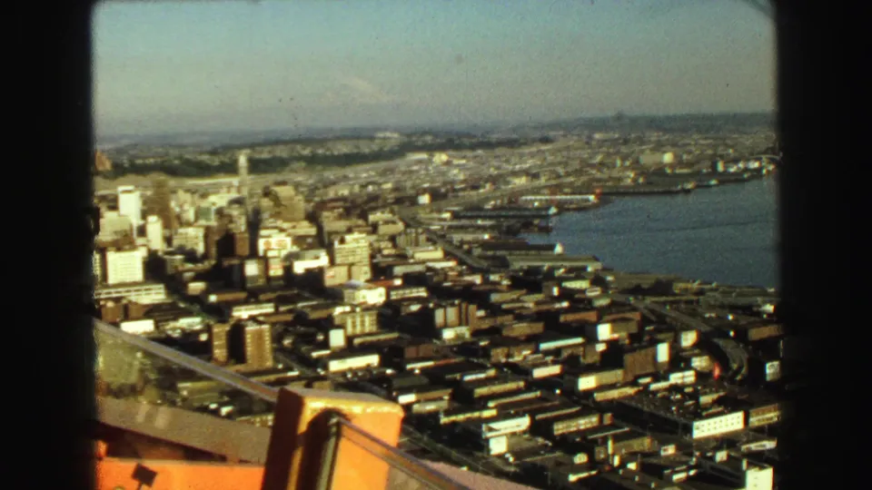 1968 Vancouver aerial frame with downtown buildings, waterfront roads, dock areas, and a broad waterway beyond.