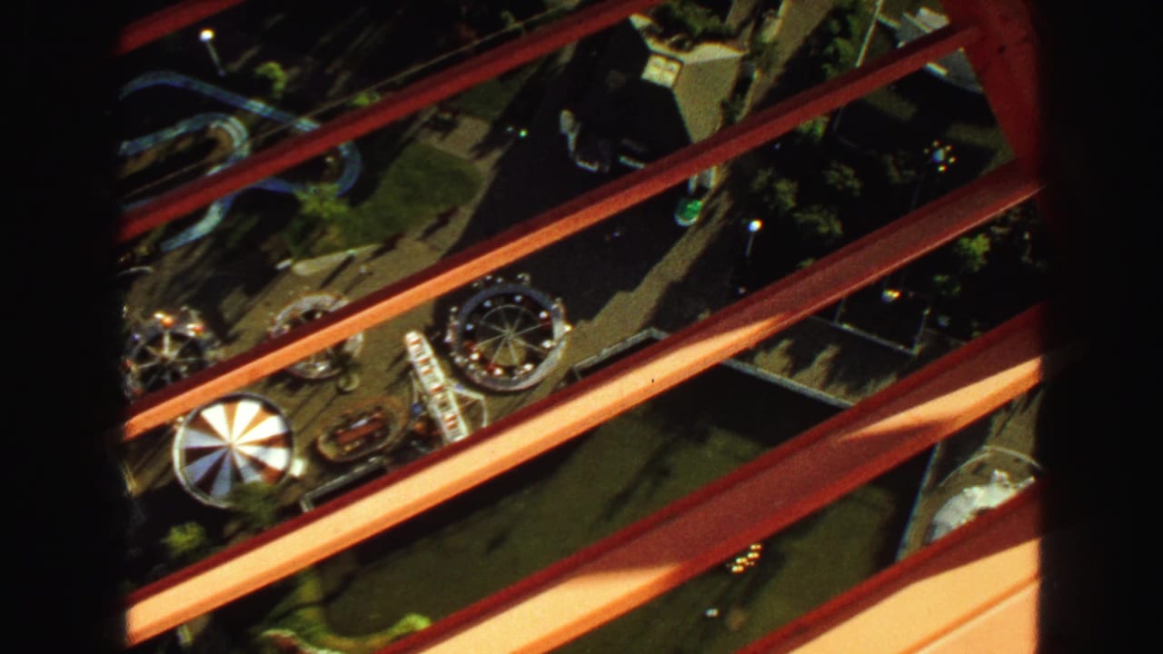 High view through red beams toward carnival rides and grounds below.