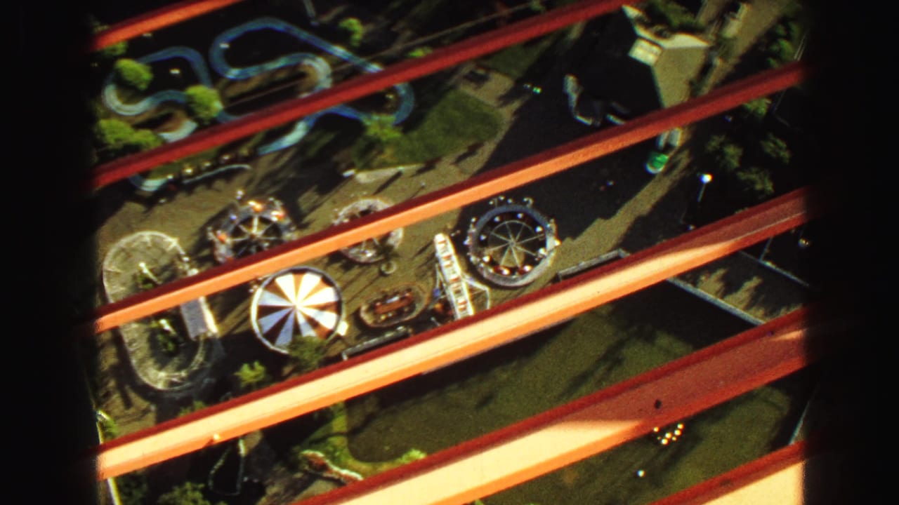 Elevated view of amusement rides below red beams and dark vertical supports.