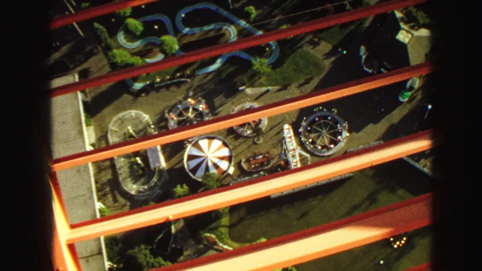 1968 Vancouver carnival grounds seen from above, with red beams, circular rides, a canopy, and winding tracks below.