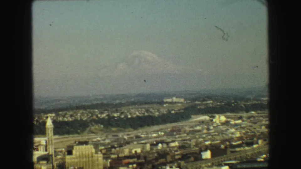 Vancouver city view with low urban buildings, a hazy sky, and a distant snow-capped mountain on the horizon.