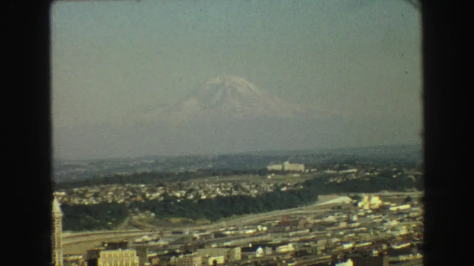 1968 8mm Vancouver-area view showing a hazy urban landscape and distant snow-covered mountain under a pale sky.