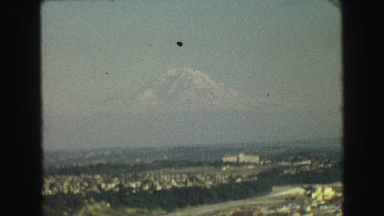 Distant mountain above a hazy cityscape with roads, buildings, and green areas.