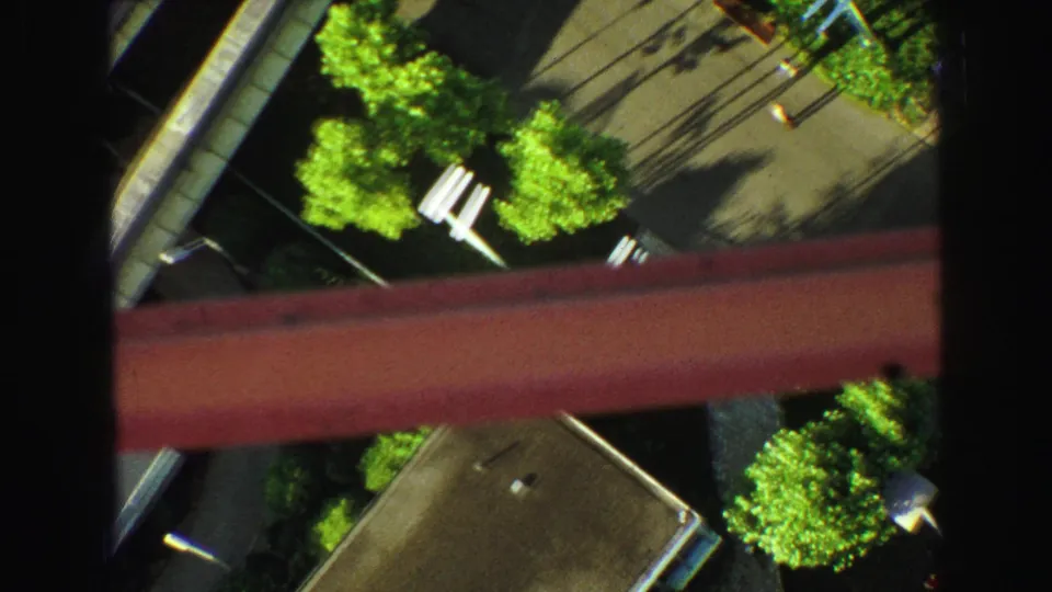 Downward-looking 1968 8mm frame from a high vantage point, showing trees, pavement, shadows, and a red structural element.