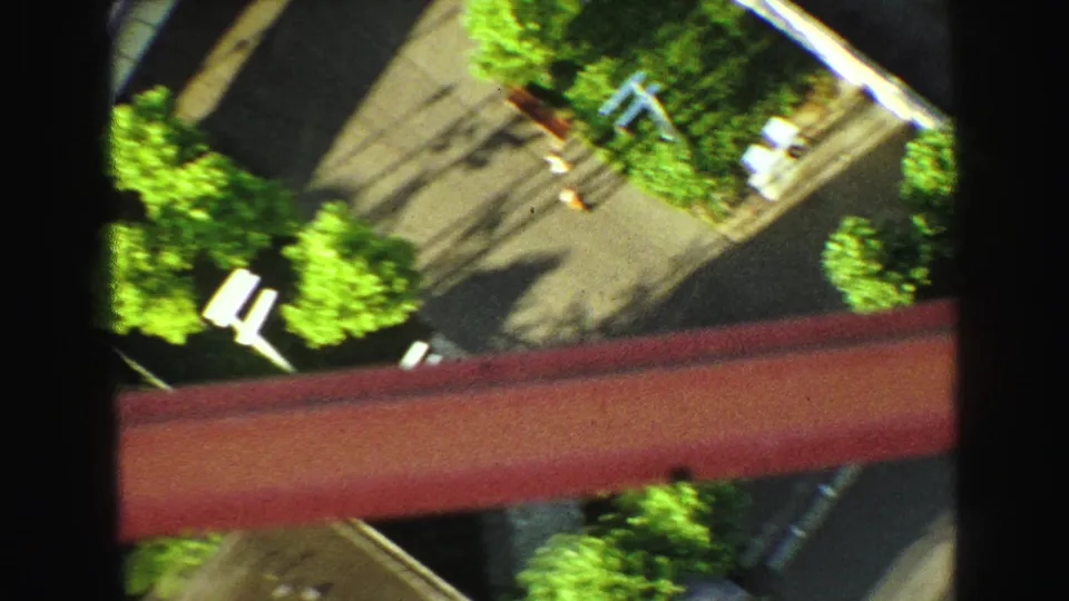 1968 8mm downward view from a high lookout or structure, with trees, pavement, shadows, and a red beam in frame.