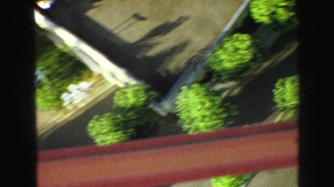 High-angle view of streets, trees, rooftops, and red beams crossing the frame.