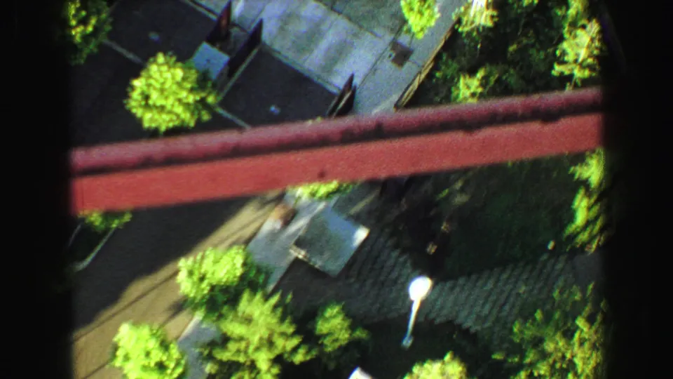 1968 Vancouver frame with a steep downward view over red beams, rooftops, trees, pavement, and a light pole.