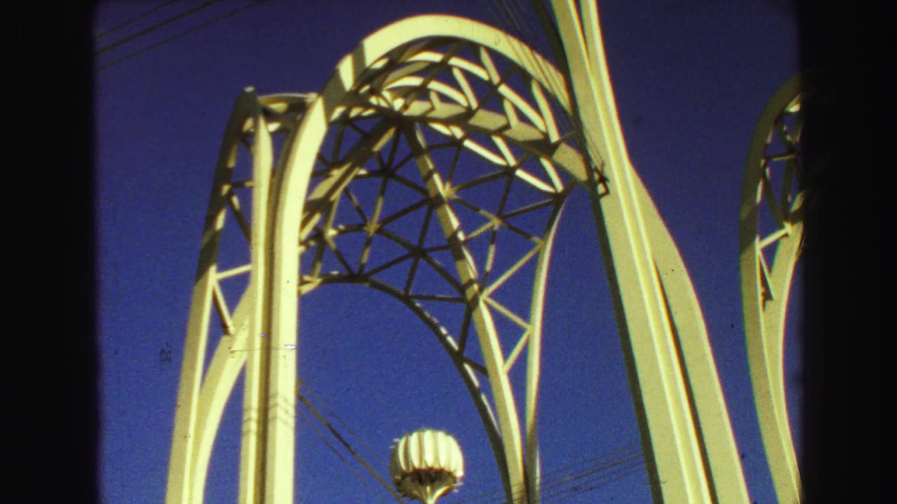 White arched architectural structure with geometric lattice against a blue sky.