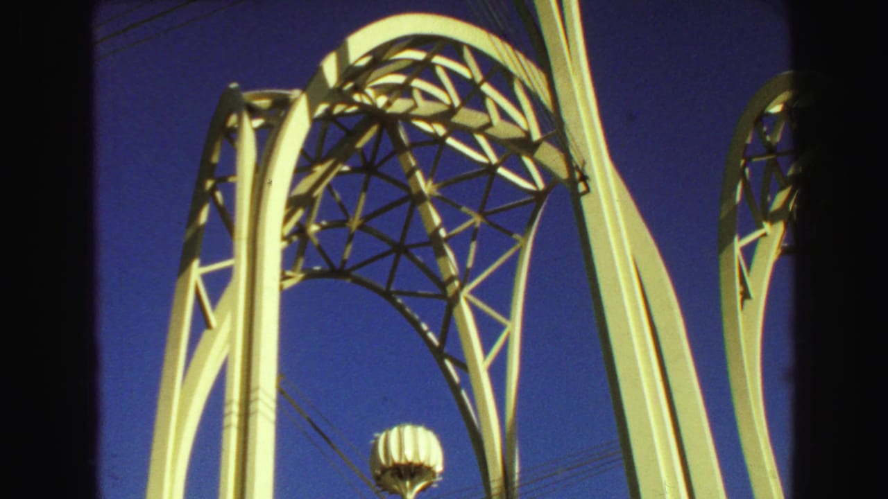 White curved structural supports and latticework seen from below against blue sky.