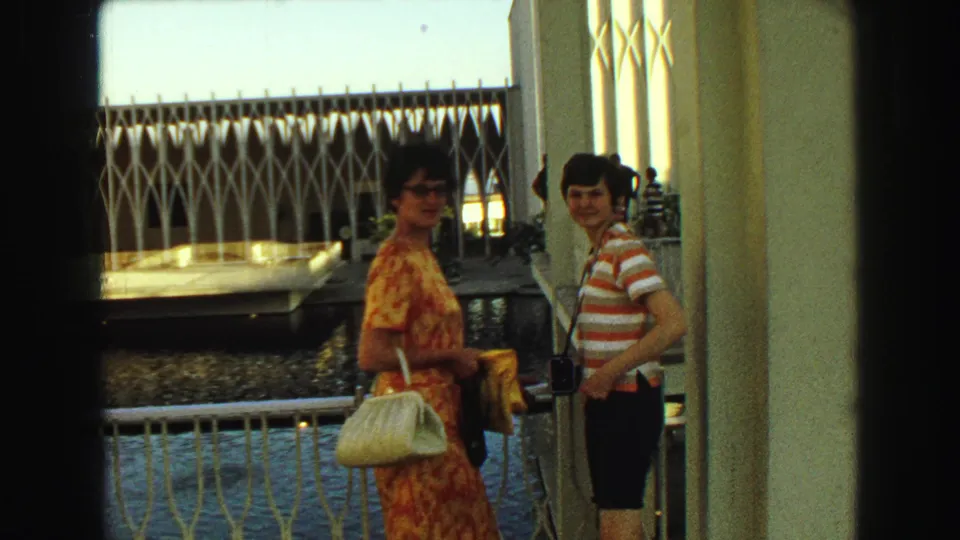 1968 Vancouver home-movie frame of two women smiling near railings, water, columns, and white geometric architecture.