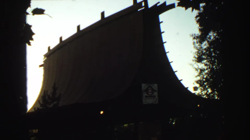 Home-movie frame of a Japanese-style roofline or gate in silhouette, with trees and a sign-like graphic near the center.
