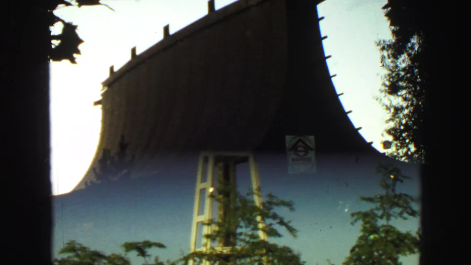Transitional 8mm frame blending a silhouetted roofline with the Space Needle tower and trees under a blue sky.