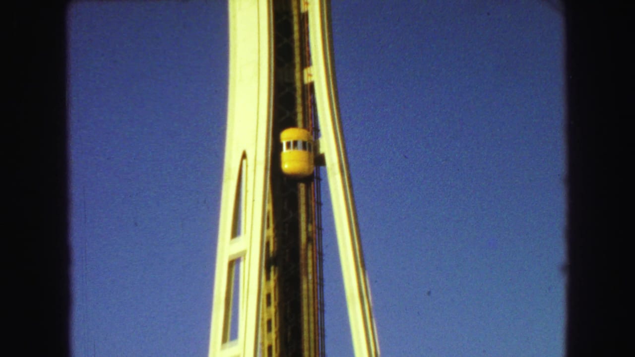 Yellow elevator car ascending along a white tower against blue sky.