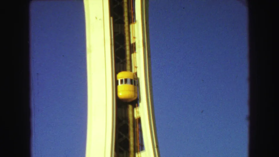 8mm frame of the yellow exterior elevator and white tower supports, cropped tightly by dark home-movie frame edges.