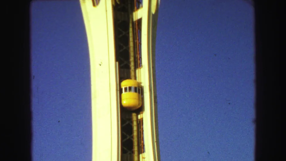 The yellow elevator continues along the exterior of the white tower, filmed in a close visitor-shot view with visible 8mm borders.