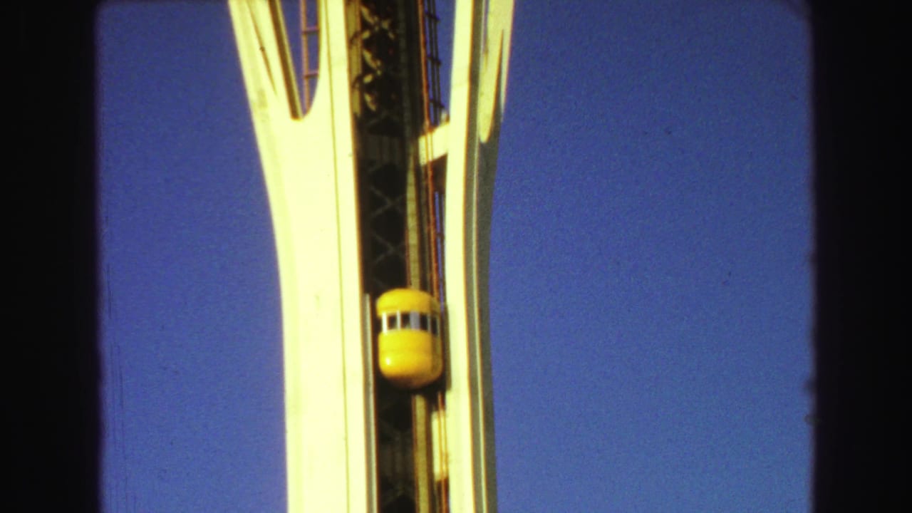Yellow elevator capsule rising between white tower supports against blue sky.