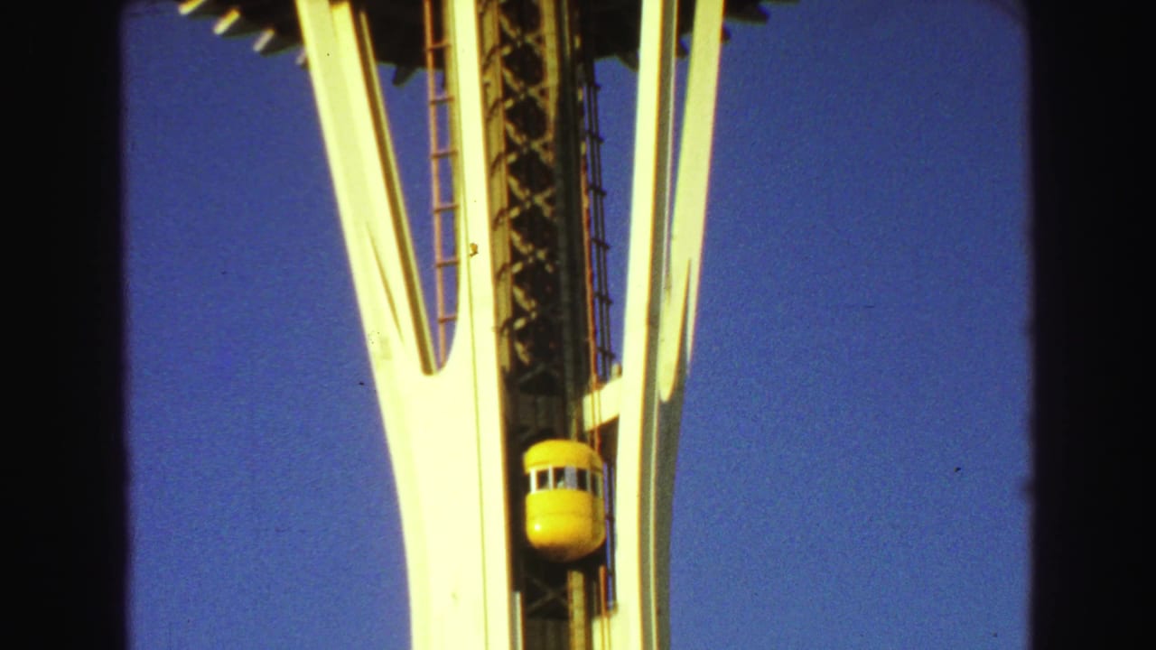 Yellow elevator capsule on the tower shaft beside white supports and blue sky.