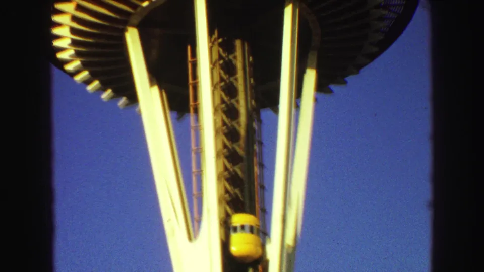1968 home-movie frame showing the tower's circular deck edge, white supports, and yellow elevator capsule viewed from below.