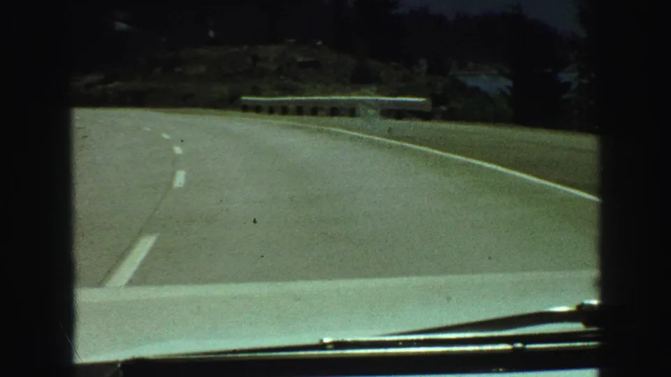 A car-mounted 8mm view shows a winding British Columbia road with a guardrail, trees, and water in the distance.