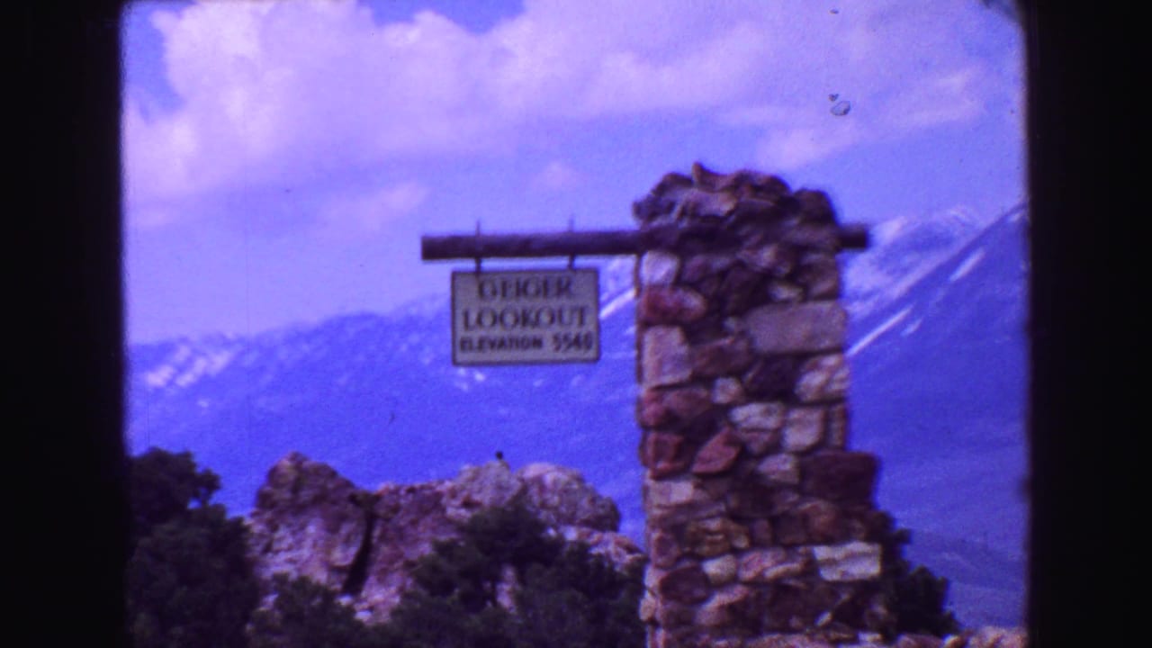 Geiger Lookout sign beside a stone pillar with mountains behind it.