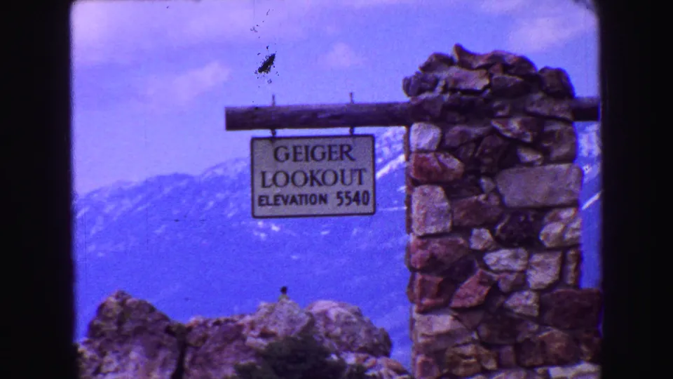 The sign reading Geiger Lookout Elevation 5540 appears beside a stone pillar, backed by hazy mountain slopes.