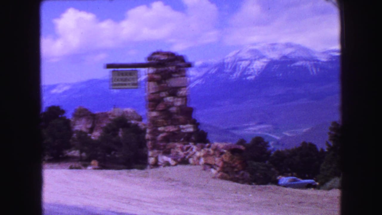 Stone roadside signpost beside a gravel turnout with snowy mountains in the distance.