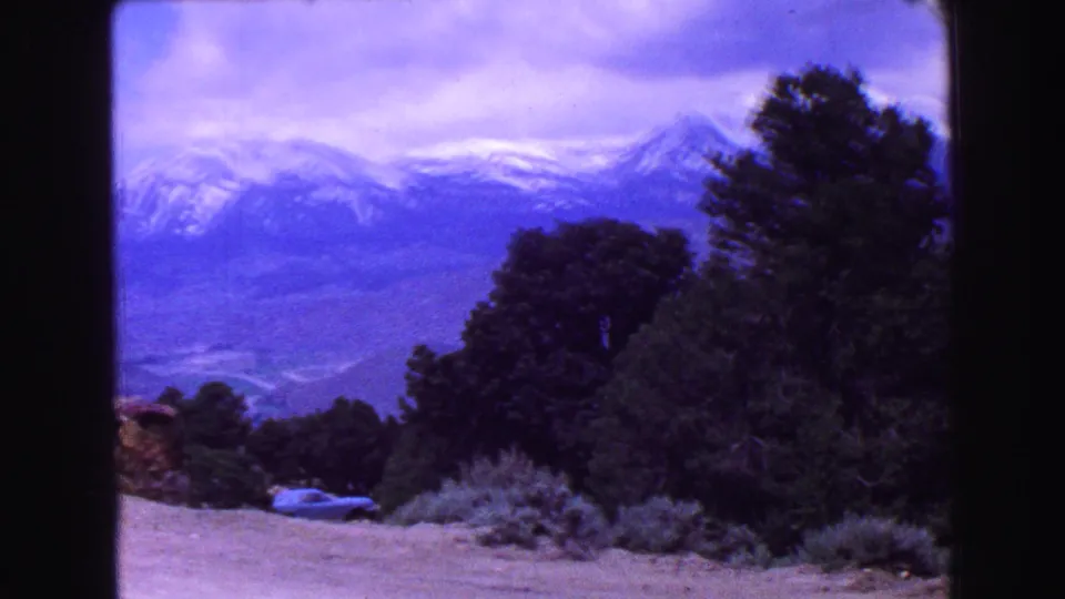 1968 Vancouver-area 8mm view across trees and brush toward a broad snow-capped mountain range.