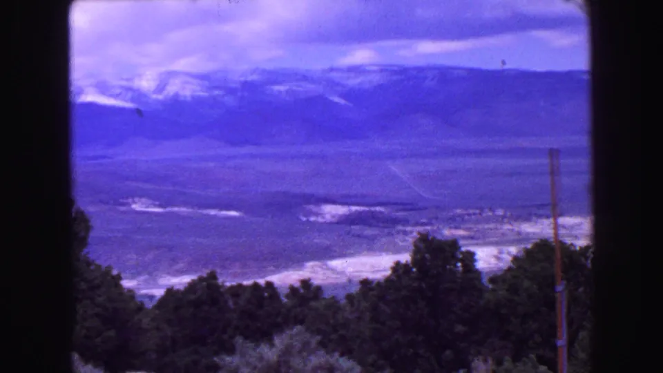 1968 Vancouver-area 8mm frame showing a broad valley, pale open areas, distant mountains, and dark treetops along the foreground.
