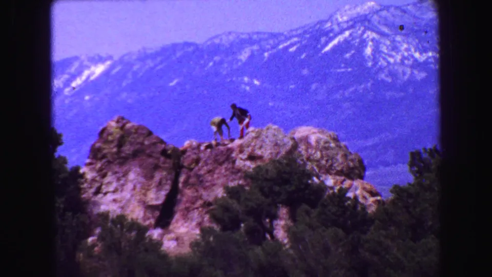 Visitors move across a rocky outcrop in a 1968 8mm mountain overlook scene near Vancouver, with a hazy snow-streaked range behind.