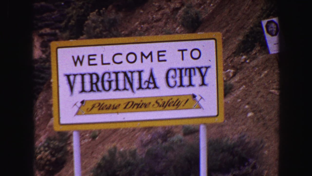 Close view of a Welcome to Virginia City sign with a safety message on a hillside roadside.