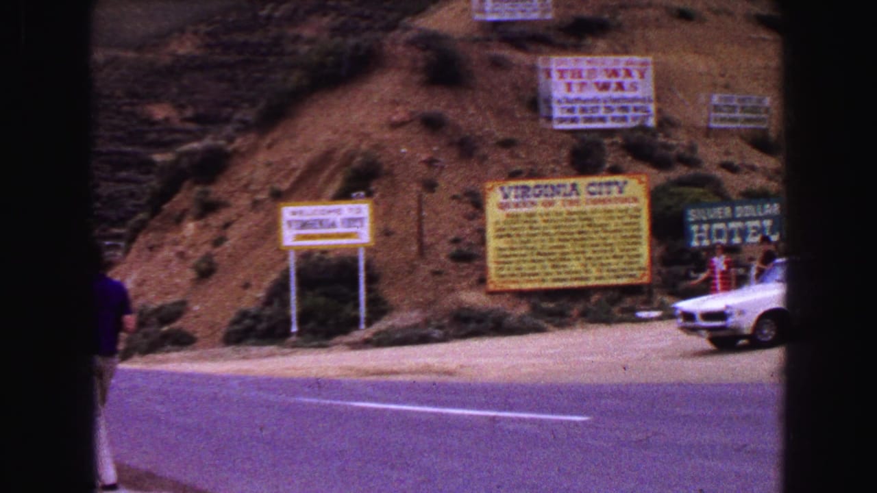 Roadside signs beside a rocky hillside with a white car partly visible.
