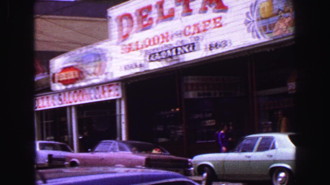 1968 Vancouver street view showing Delta Saloon & Cafe signage, parked classic cars, and a few pedestrians near storefronts.