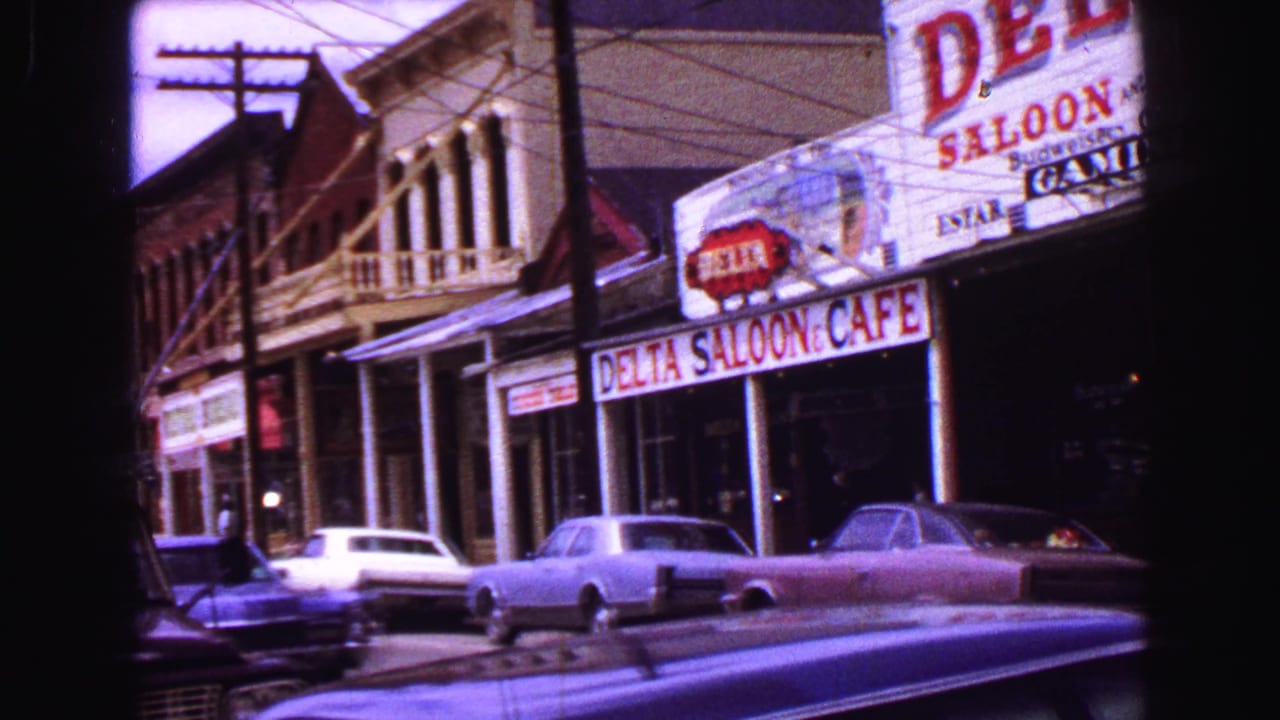 1968 Vancouver commercial block with Delta Saloon & Cafe signage, a second-floor balcony facade, utility wires, and 1960s cars.