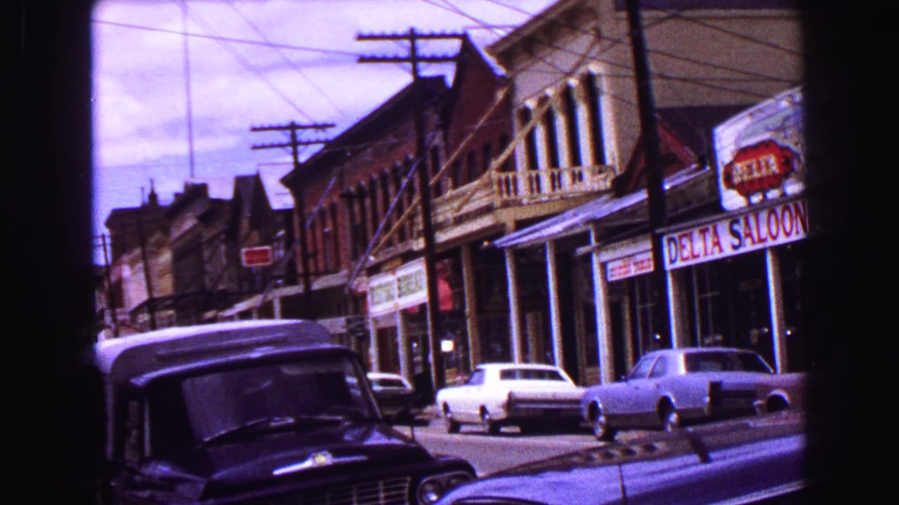 1968 Vancouver street scene with Delta Saloon storefront, neighboring commercial buildings, utility lines, and parked classic cars.