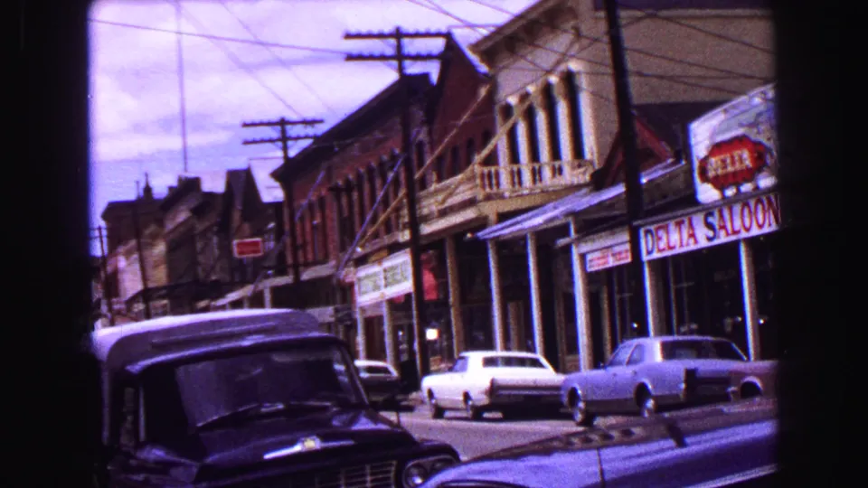 1968 Vancouver street scene with Delta Saloon storefront, neighboring commercial buildings, utility lines, and parked classic cars.