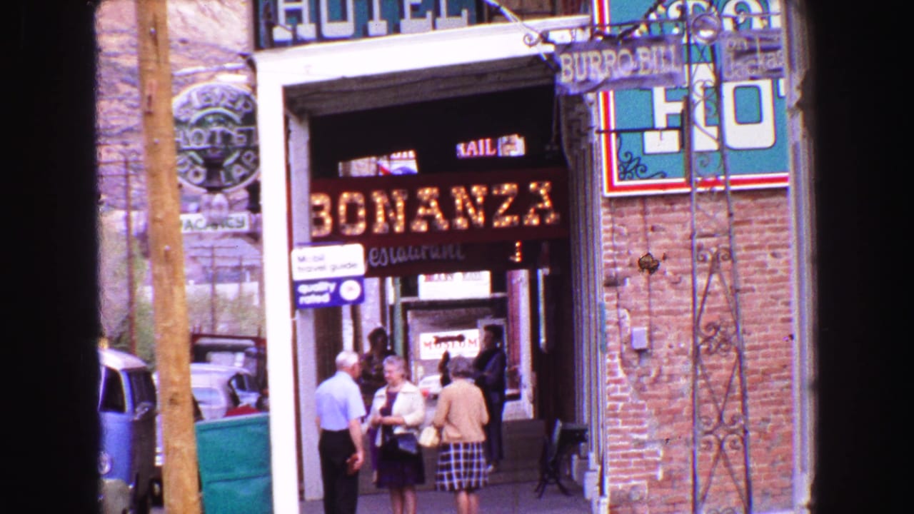 Close 1968 Vancouver street view showing Bonanza restaurant signage, people near the doorway, a hotel sign, brick walls, and parked cars.