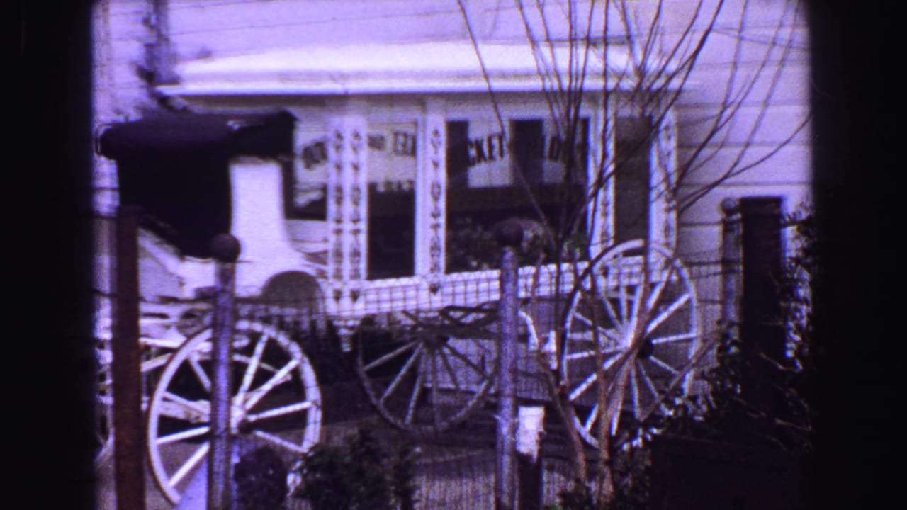 1968 Vancouver home-movie frame showing a white vintage buggy display, wagon wheels, bare trees, and ornate storefront trim.