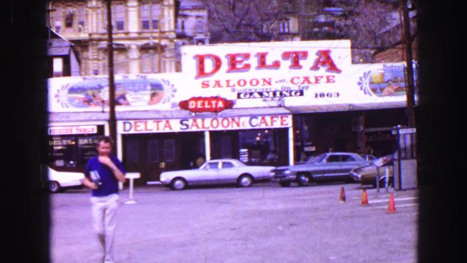 1968 Vancouver street view of Delta Saloon and Cafe signage, parked cars, older facades, traffic cones, and a pedestrian.