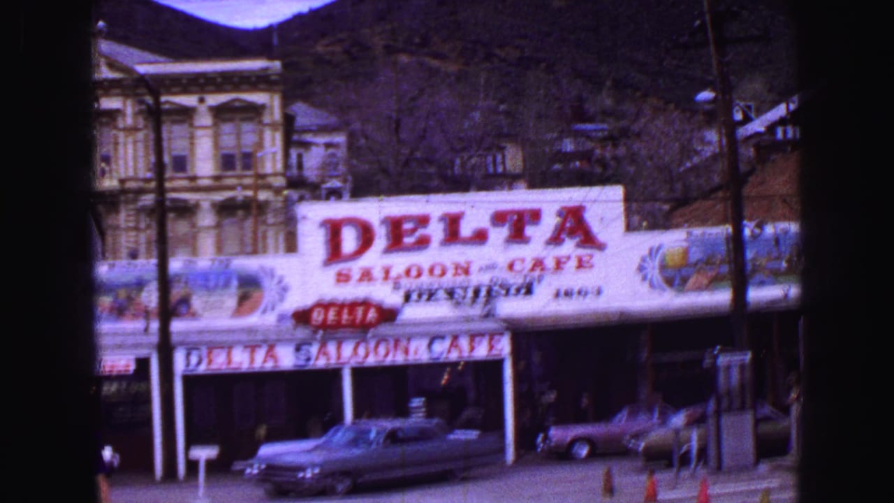 Delta Saloon & Cafe storefront with parked cars, utility poles, and hills behind it.