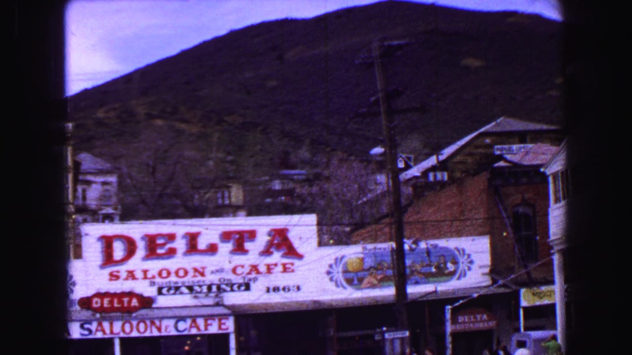 Delta Saloon & Cafe sign seen across a street with mountains and utility lines behind it.
