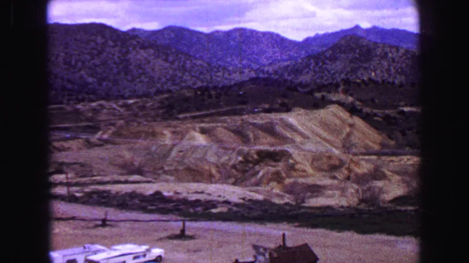 1968 8mm frame of dry, scrub-covered hills and rugged mountains, filmed from an elevated or roadside viewpoint.