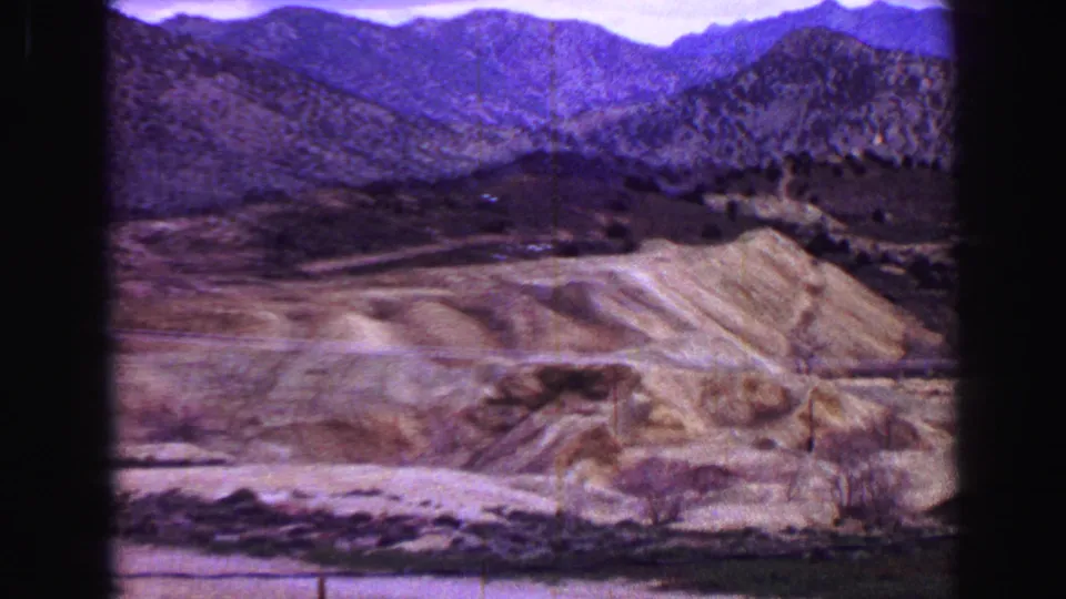 1968 8mm frame showing arid slopes, scrub cover, and rugged mountain ridges in a broad valley view.