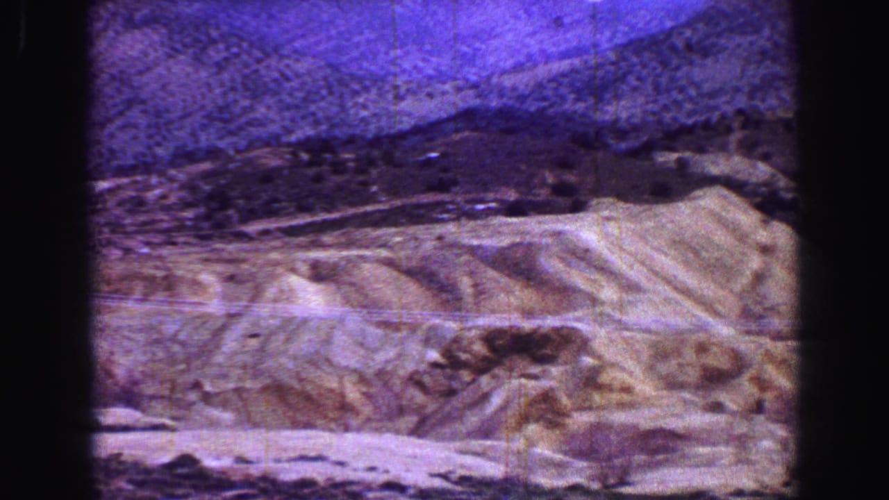 Dry hillside with distant purple mountains seen through dark film gate edges.