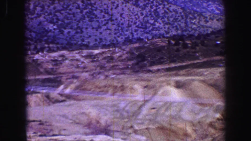 A moving 8mm view of rugged hills, sparse vegetation, and power lines with mountains in the background near Vancouver, British Columbia.
